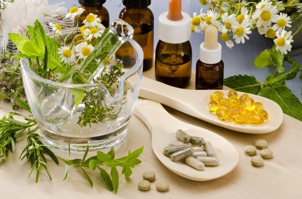 Herbs in mortar, bottles with droppers, pills and capsules on wooden spoons, chamomile flowers — All Body Holistic Health in Thuringowa Central, QLD
