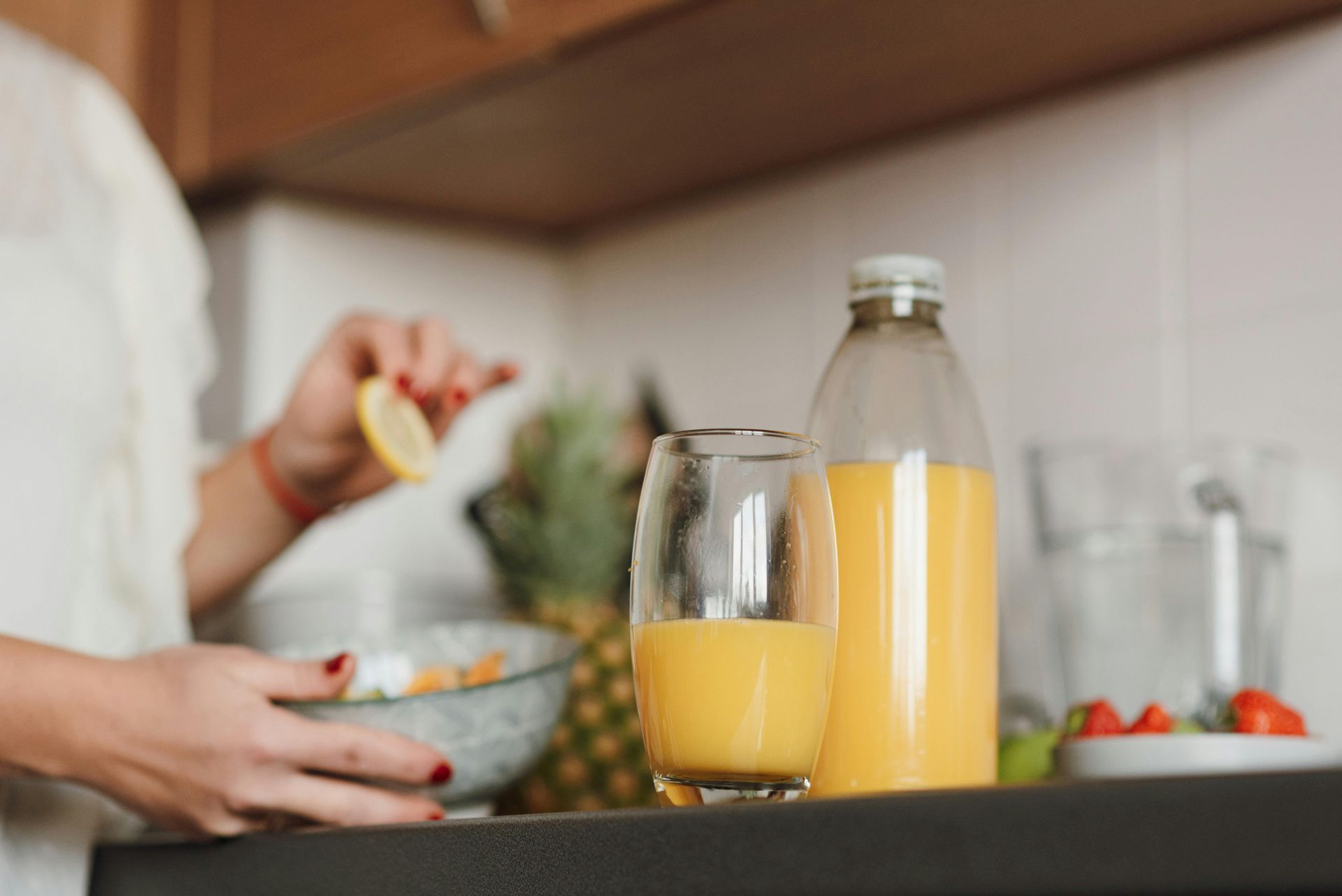 Woman squeezing lemon into a glass of juice. A full juice bottle, fruit, and salad are on the counter — All Body Holistic Health in Thuringowa Central, QLD