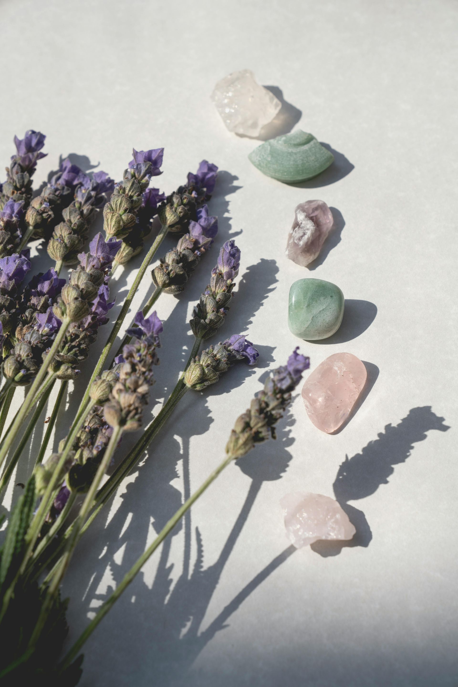 Lavender sprigs beside various pastel-coloured tumbled stones on a white surface  — All Body Holistic Health in Thuringowa Central, QLD