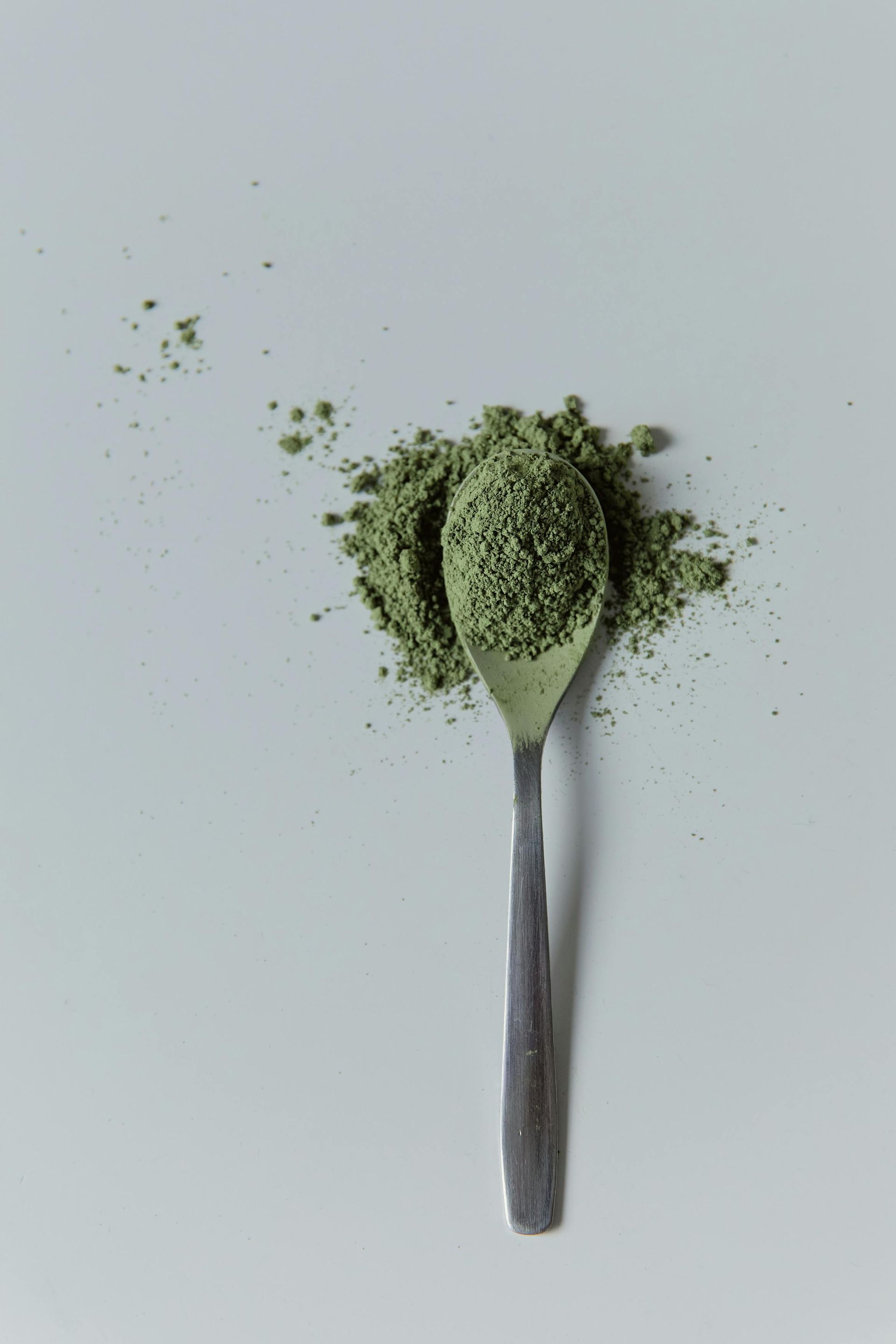 Spoonful of green powder spilling onto a white surface — All Body Holistic Health in Thuringowa Central, QLD