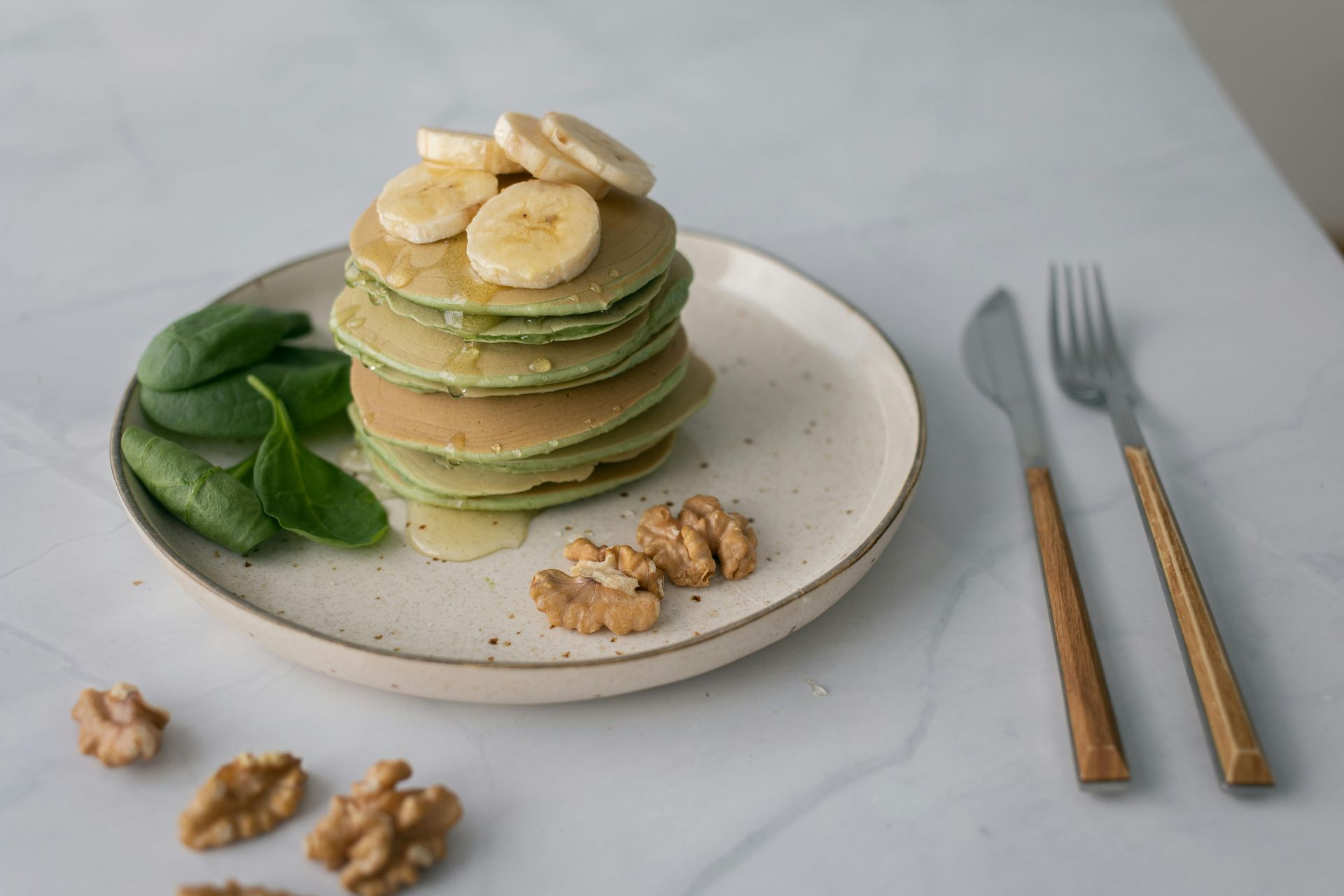 Green pancakes with banana slices, spinach, walnuts, and utensils on a plate — All Body Holistic Health in Thuringowa Central, QLD