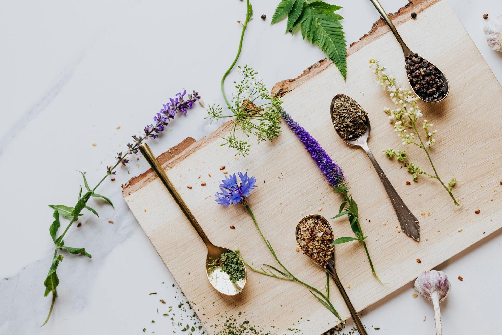 Wooden board with spoons of herbs and flowers on a white surface — All Body Holistic Health in Thuringowa Central, QLD