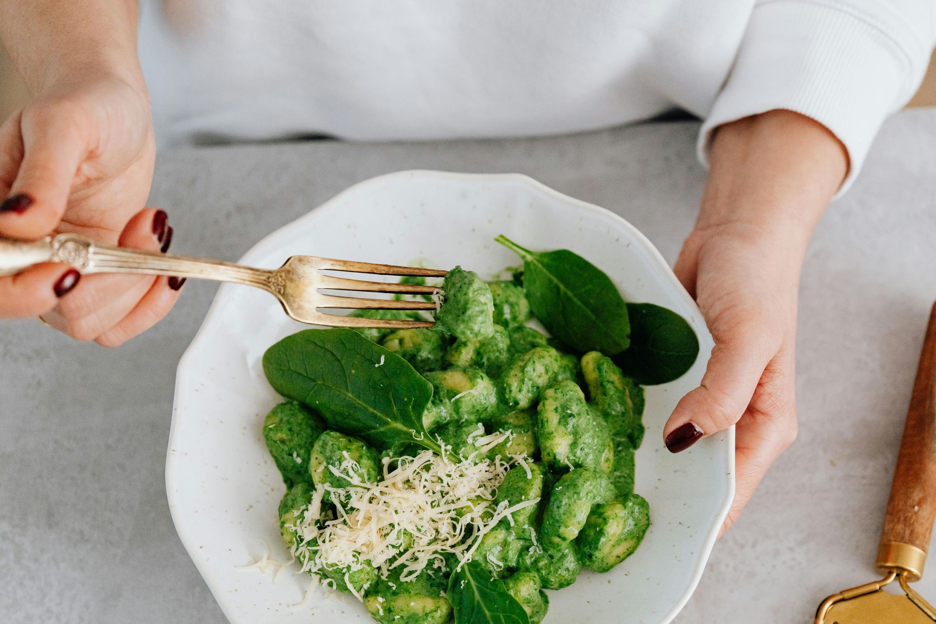 Person eating gnocchi with spinach and cheese from a white plate. Hands holding a fork — All Body Holistic Health in Thuringowa Central, QLD