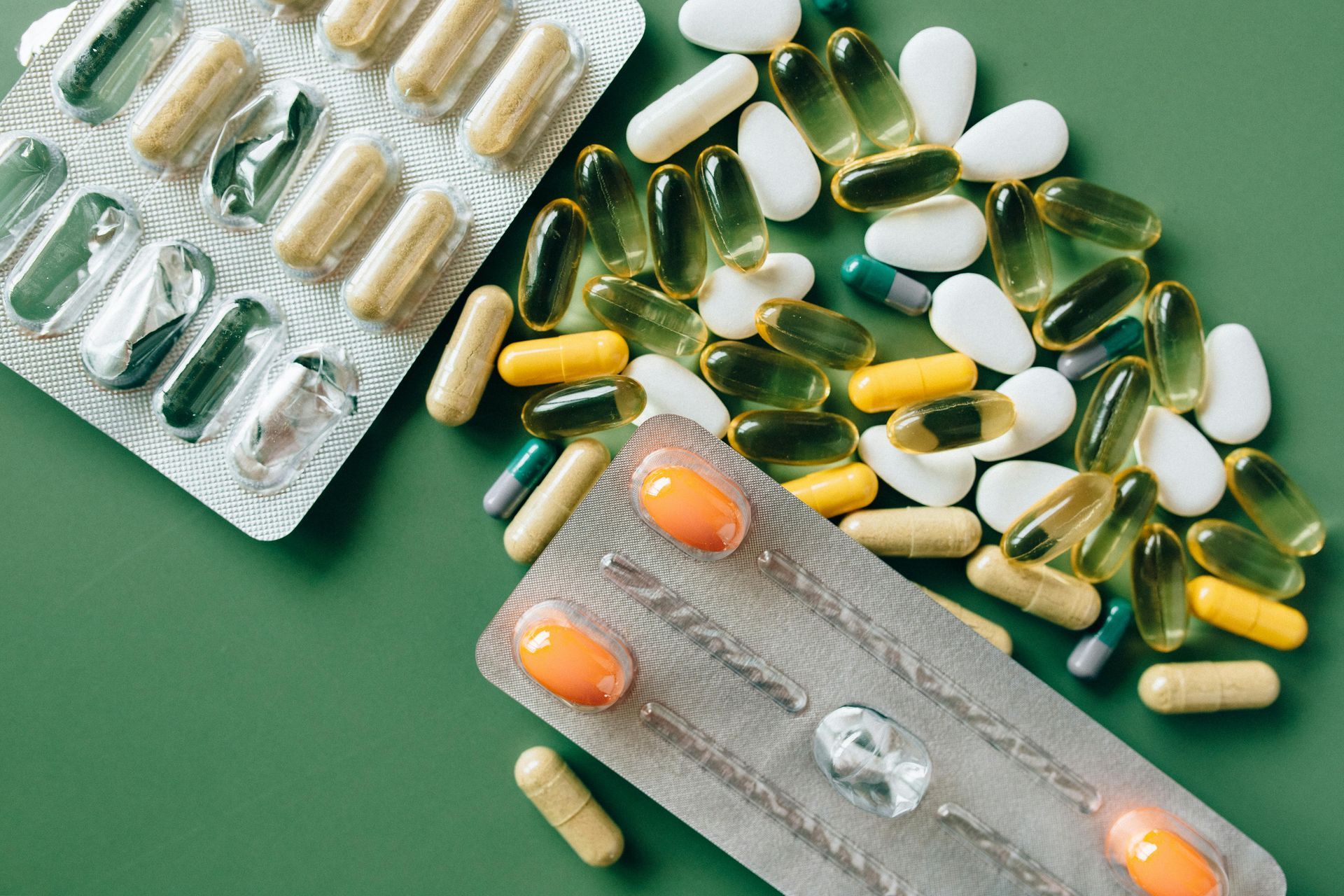 Pills and capsules of various colours scattered on a green surface with two blister packs — All Body Holistic Health in Thuringowa Central, QLD