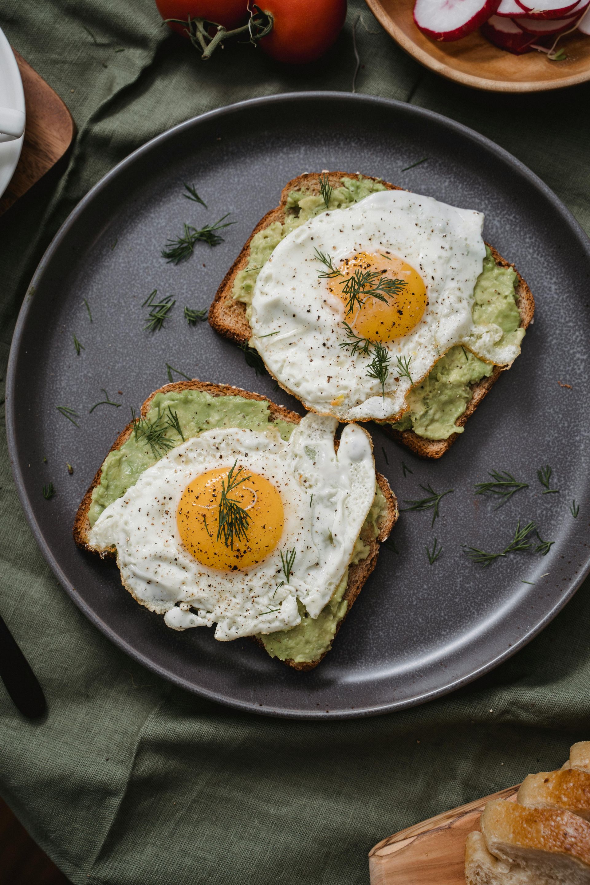 Two avocado toasts topped with fried eggs on a dark plate, garnished with dill — All Body Holistic Health in Thuringowa Central, QLD