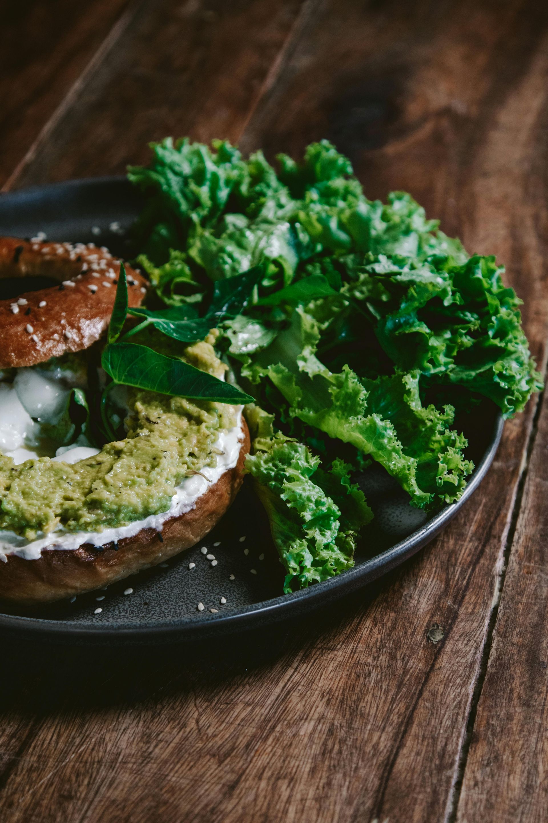 Bagel with green spread and lettuce on a dark plate, placed on a wooden table — All Body Holistic Health in Thuringowa Central, QLD