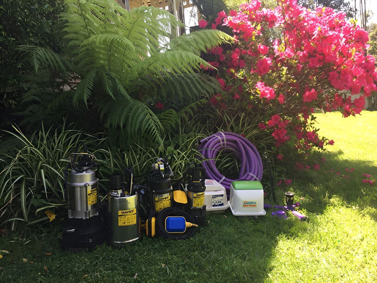 Tools Are Sitting on the Grass Next to a Bush With Pink Flowers — All Systems Wastewater Maintenance In Jilliby, NSW