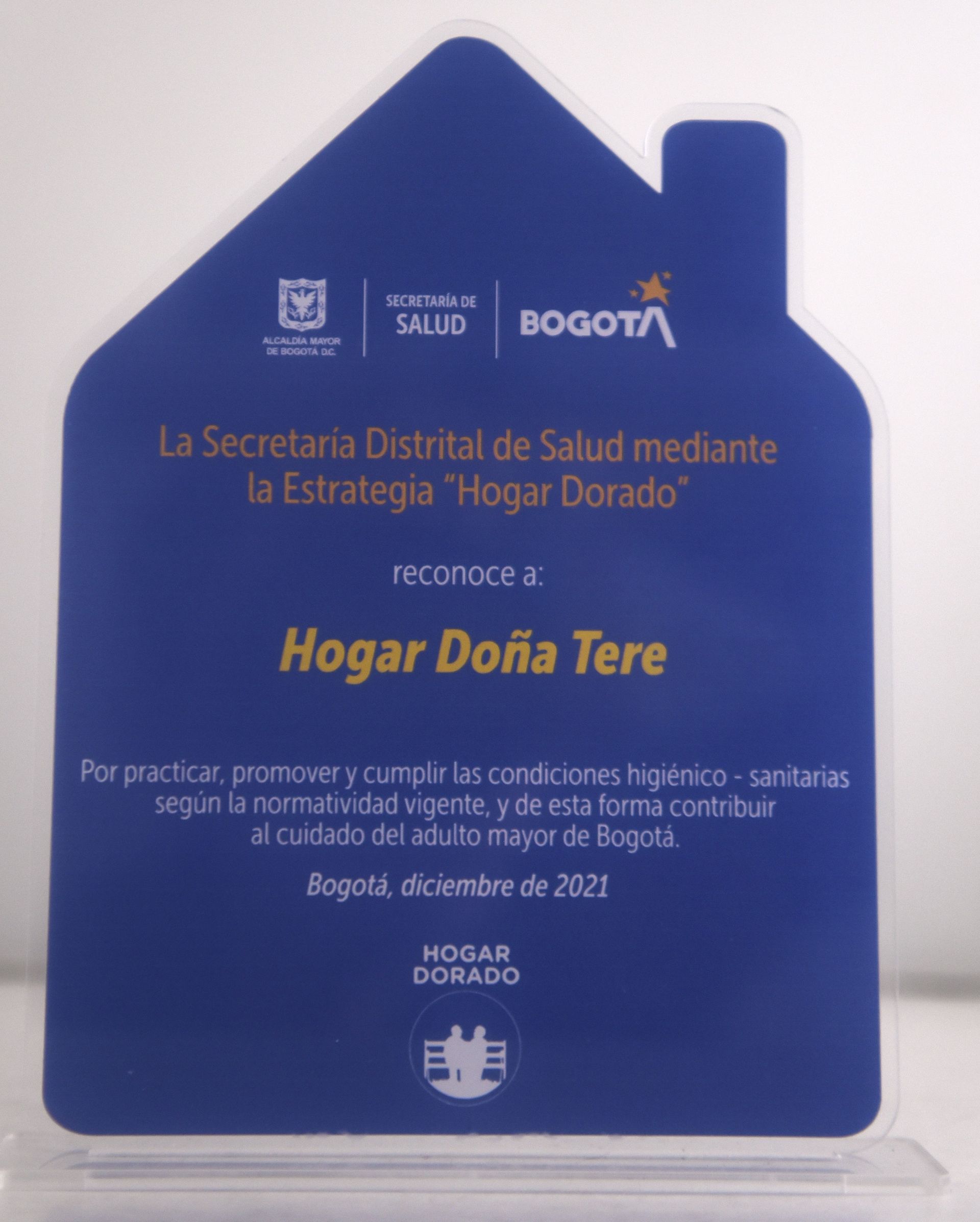 Placa en forma de casa azul, “Hogar Doña Tere” otorgada por la secretaría de salud de Bogotá por prácticas sanitarias.