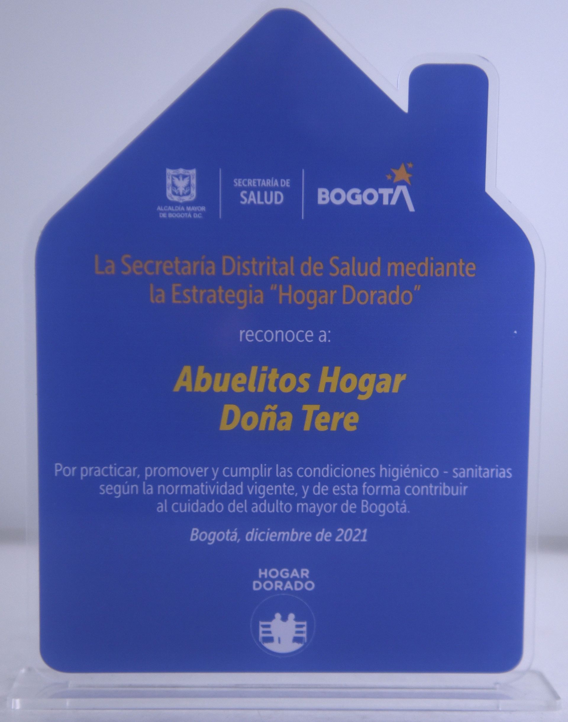 Premio azul en forma de casa, con texto en reconocimiento a “Abuelitos Hogar Doña Tere” por la atención en salud en Bogotá.