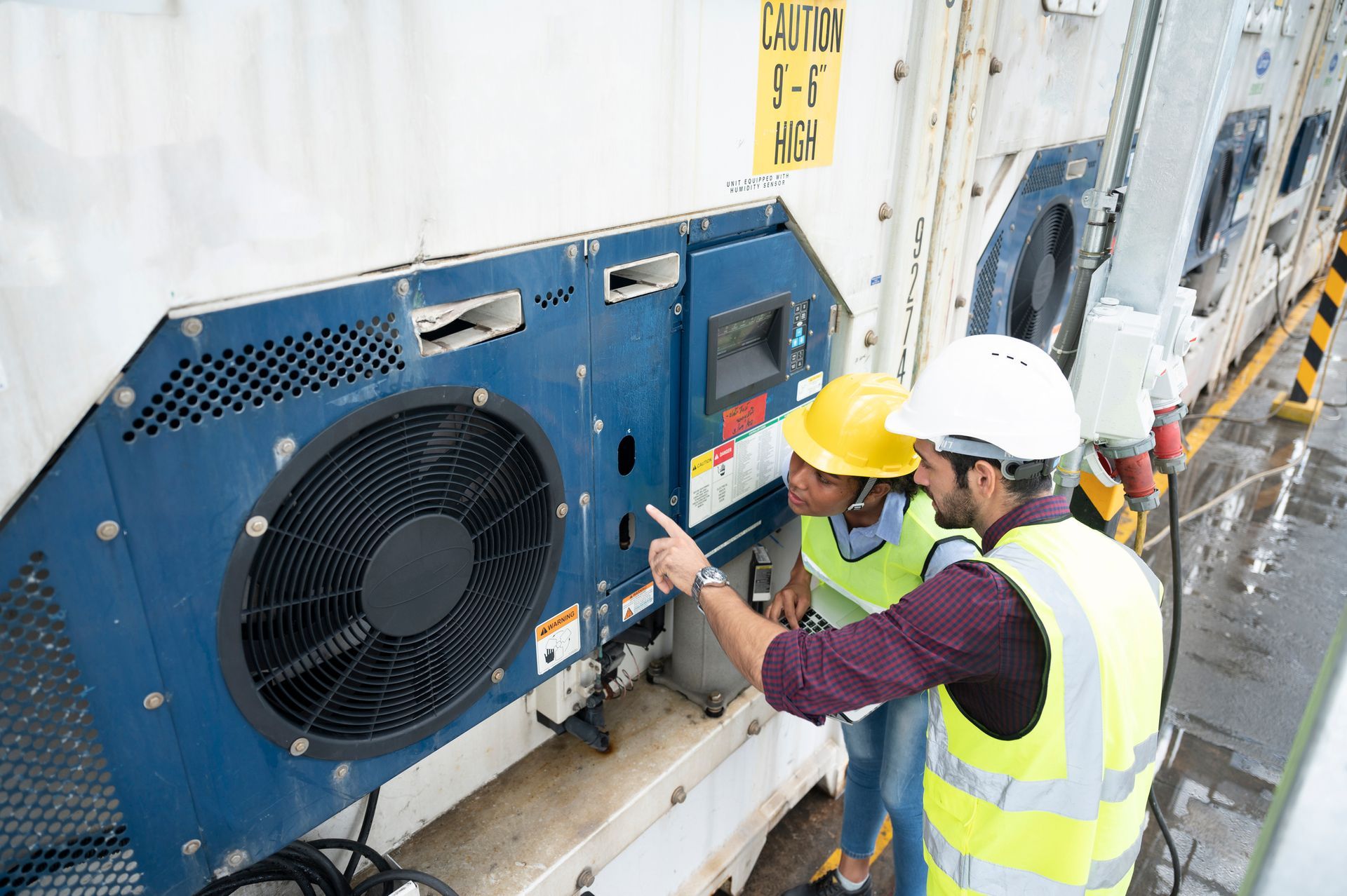 Two construction workers are looking at a fan on a container.