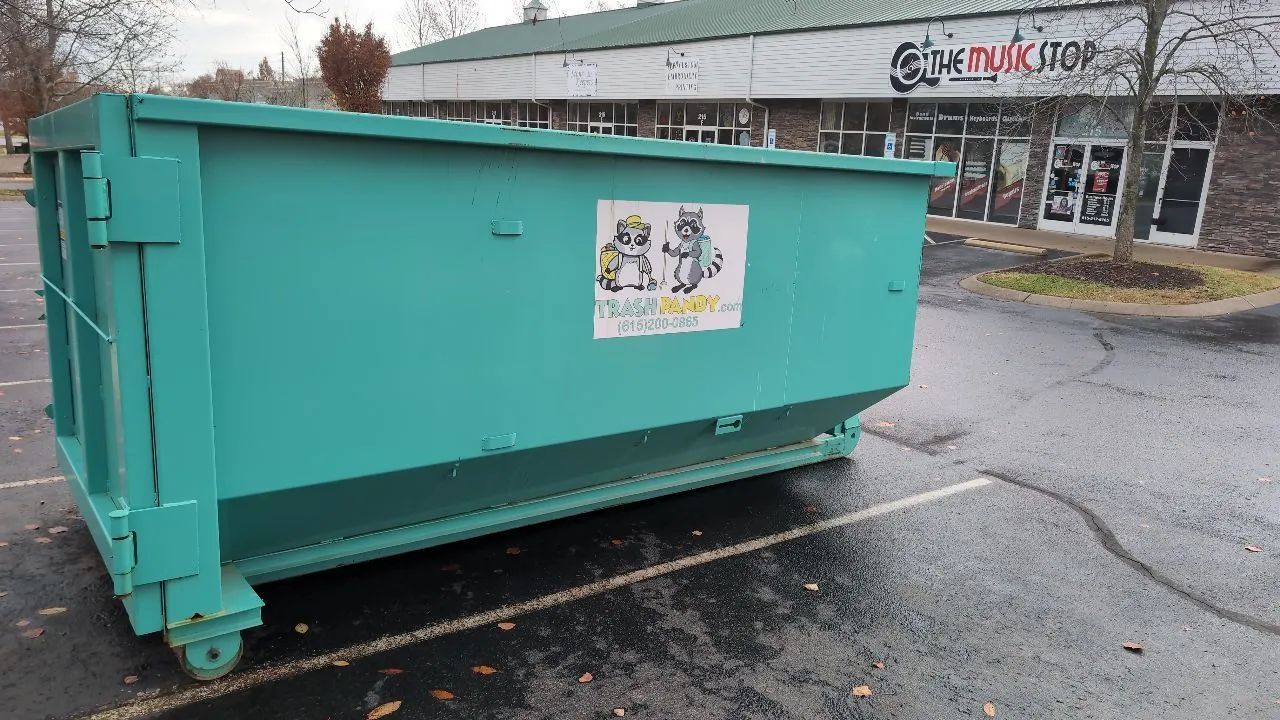 Green dumpster in a parking lot, near a store.
