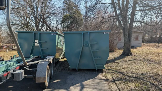 A pile of wood and metal is sitting in front of a dumpster.