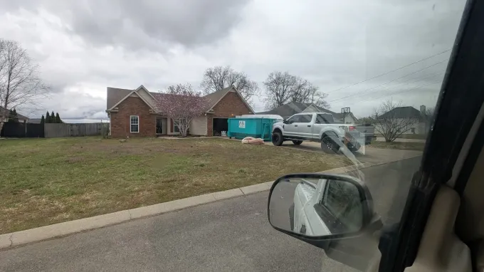 A dumpster is parked in front of a blue house covered in snow.