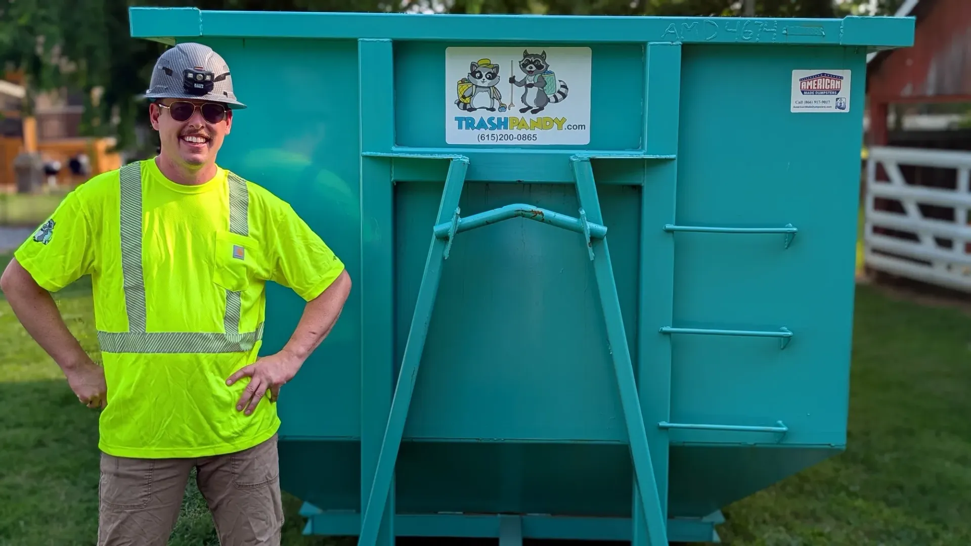 A green dumpster with a yellow lid is sitting on top of a gravel road.