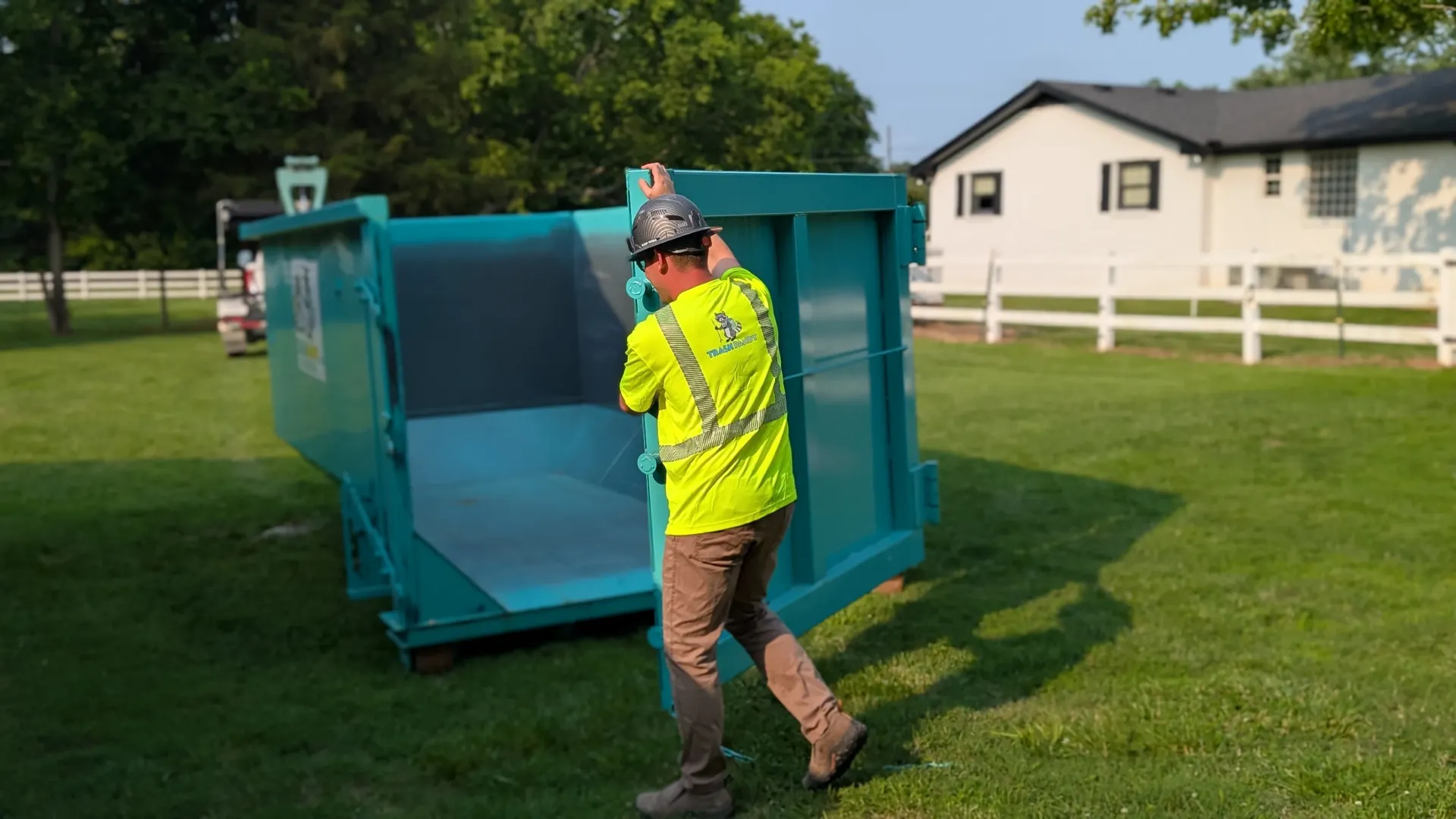 A man is pushing a dumpster in a grassy field.