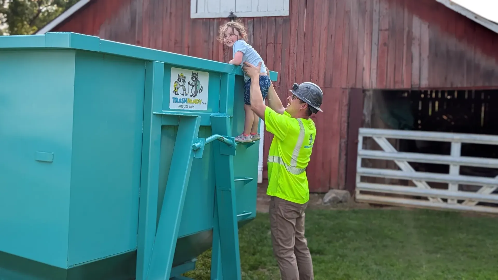 A green dumpster with a yellow lid is sitting on top of a gravel road.
