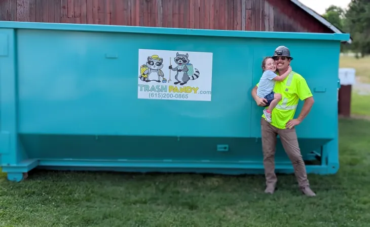 A white garbage truck with a green dumpster attached to it is parked in a parking lot.