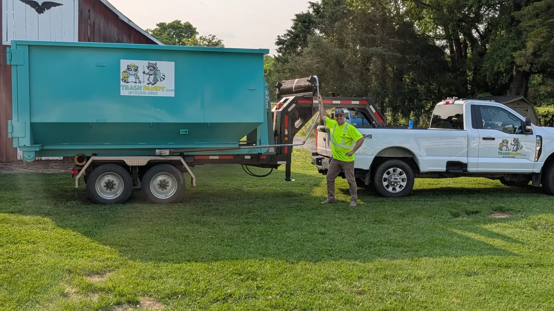 A man is standing next to a dumpster and a truck.