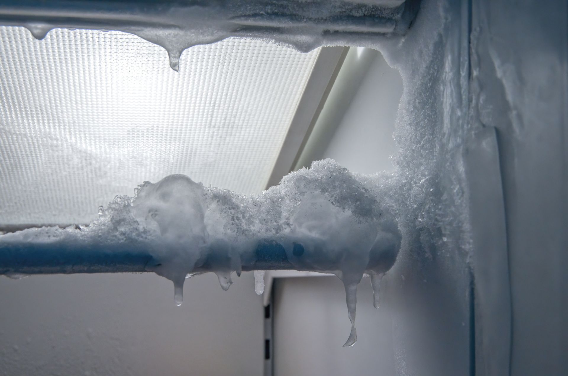 A close up of a frozen refrigerator door with icicles hanging from it.