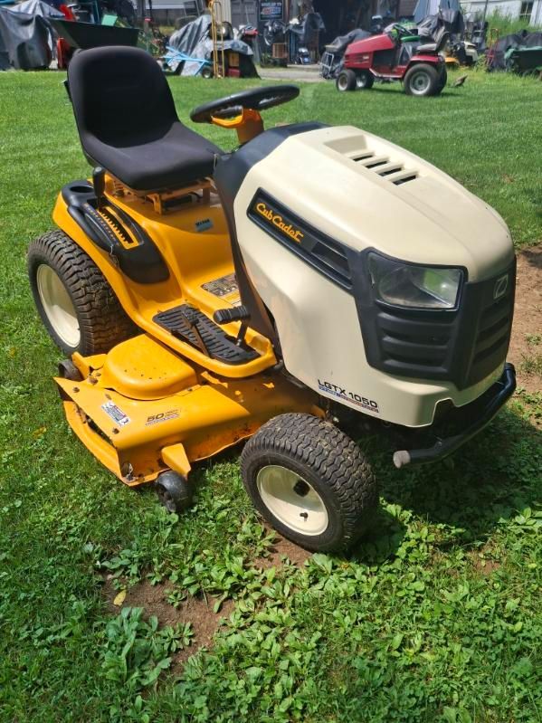 Yellow Cub Cadet riding lawnmower on green grass, with beige hood, black seat, and another mower in the background.