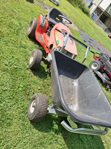 Red riding lawn mower with a black wheelbarrow attached on green grass.
