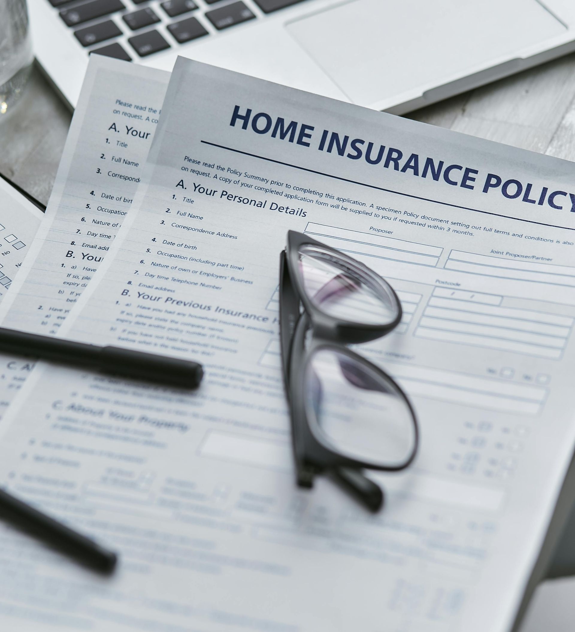 Home insurance policy document with glasses and a pen on a desk near a laptop.