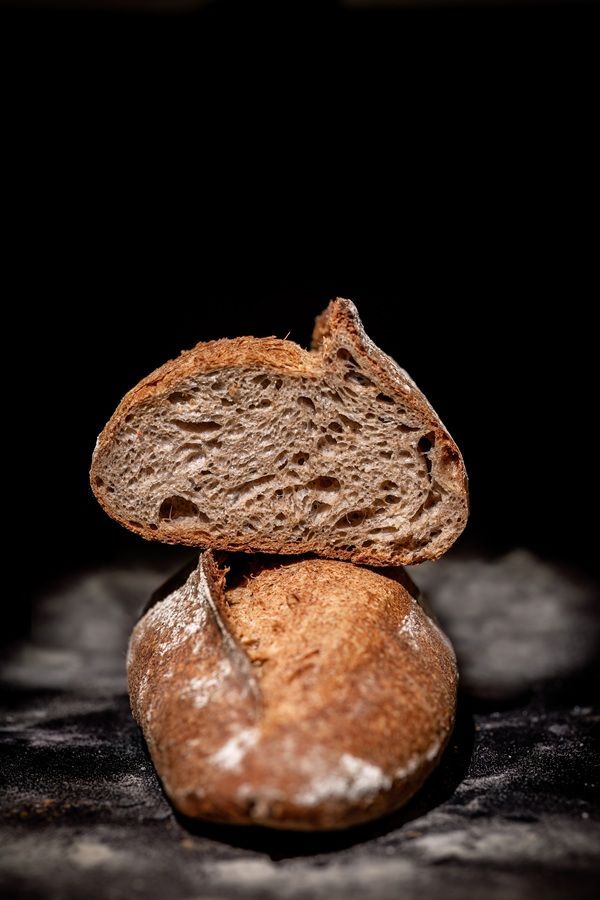 Pane rustico a fette impilato su una pagnotta intera su uno sfondo scuro