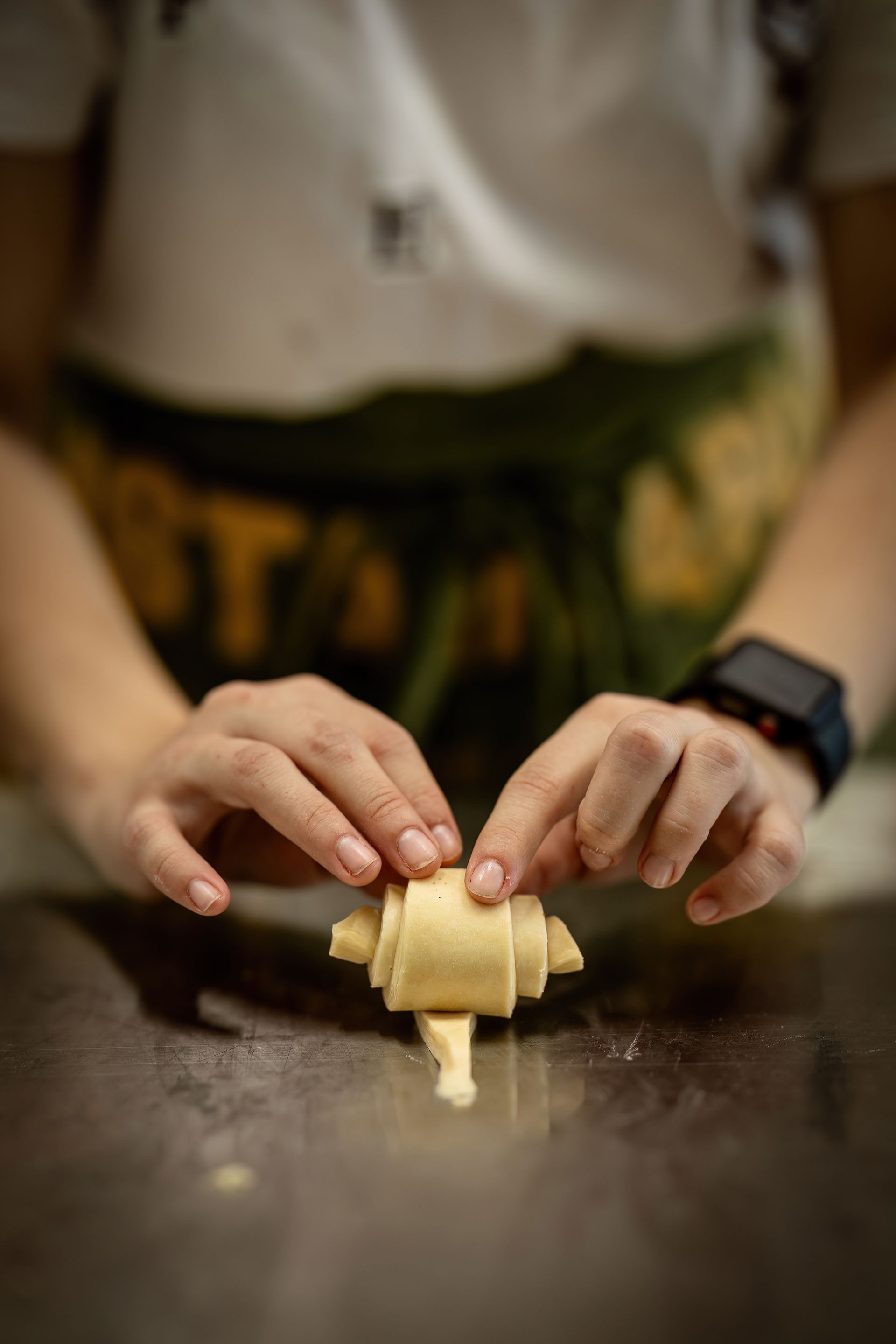 Mani che stendono la pasta su un piano di lavoro scuro, con uno smartwatch nero ben visibile.