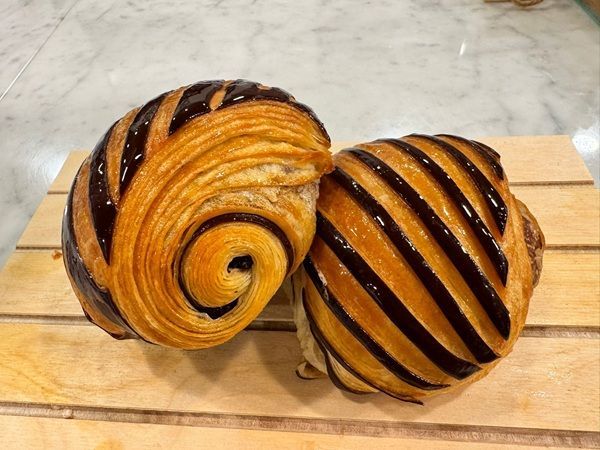 Due pasticcini a spirale, uno dorato e uno a strisce scure, su un vassoio di legno.