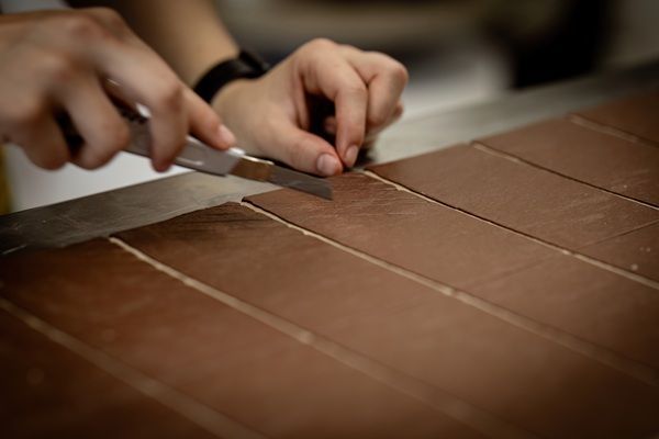 Mani che tagliano a strisce un foglio marrone con un coltello su un tavolo da lavoro