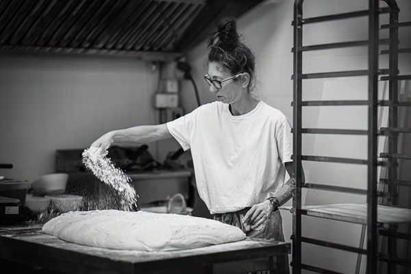 In un panificio, una persona modella l'impasto su un tavolo da lavoro, con scaffali impilati sullo sfondo.