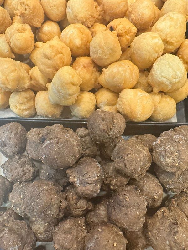 Vassoi di snack fritti dorati e scuri impilati in una vetrina gastronomica.