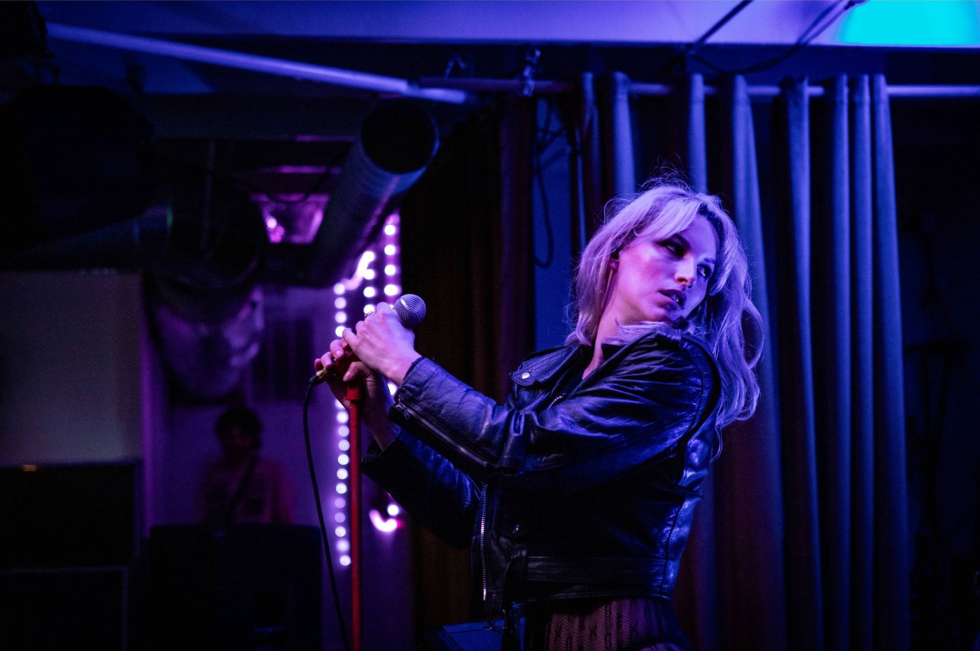 A woman in a leather jacket is singing into a microphone on a stage.