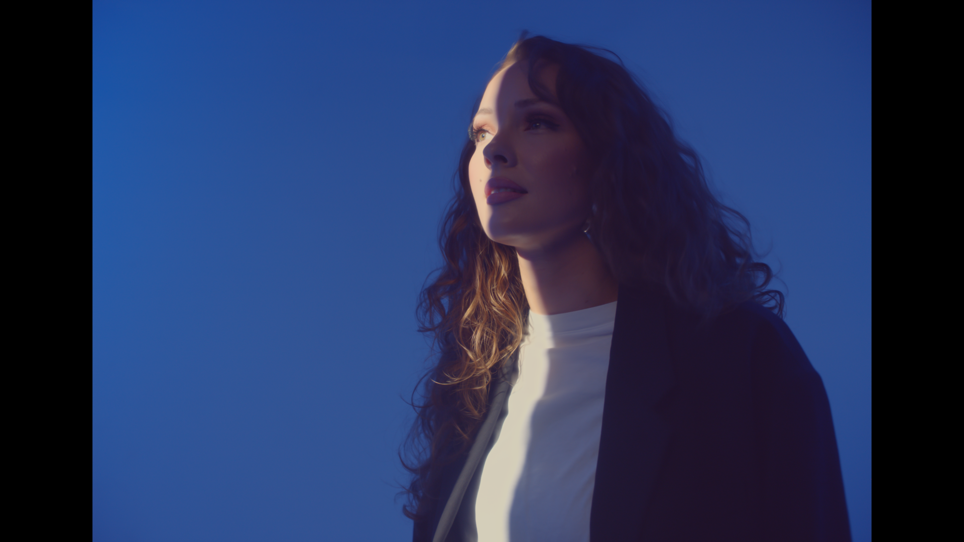 A woman with long hair is standing in front of a blue sky.