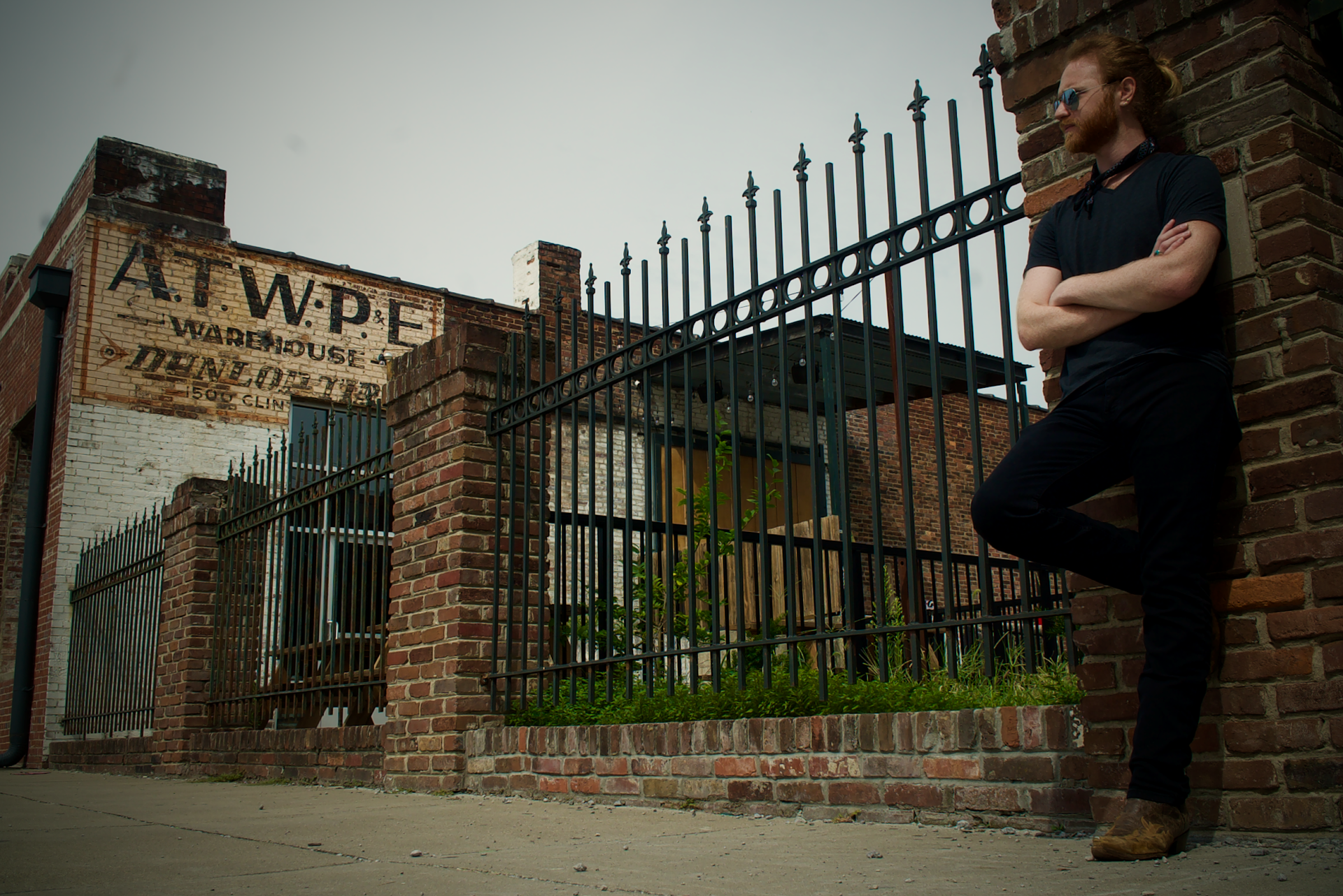 A man leaning against a brick wall with his arms crossed.