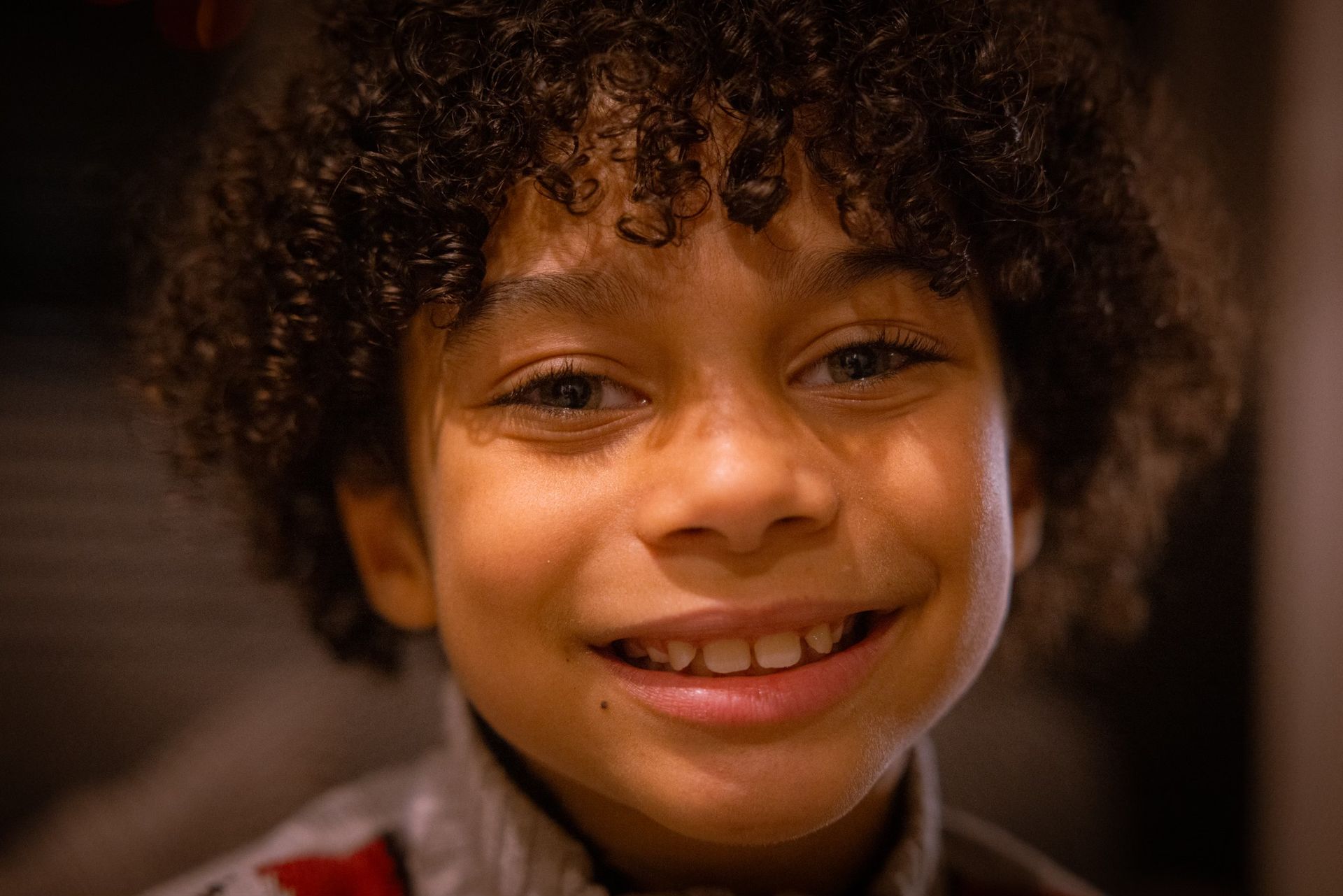 A young boy with curly hair is smiling for the camera.