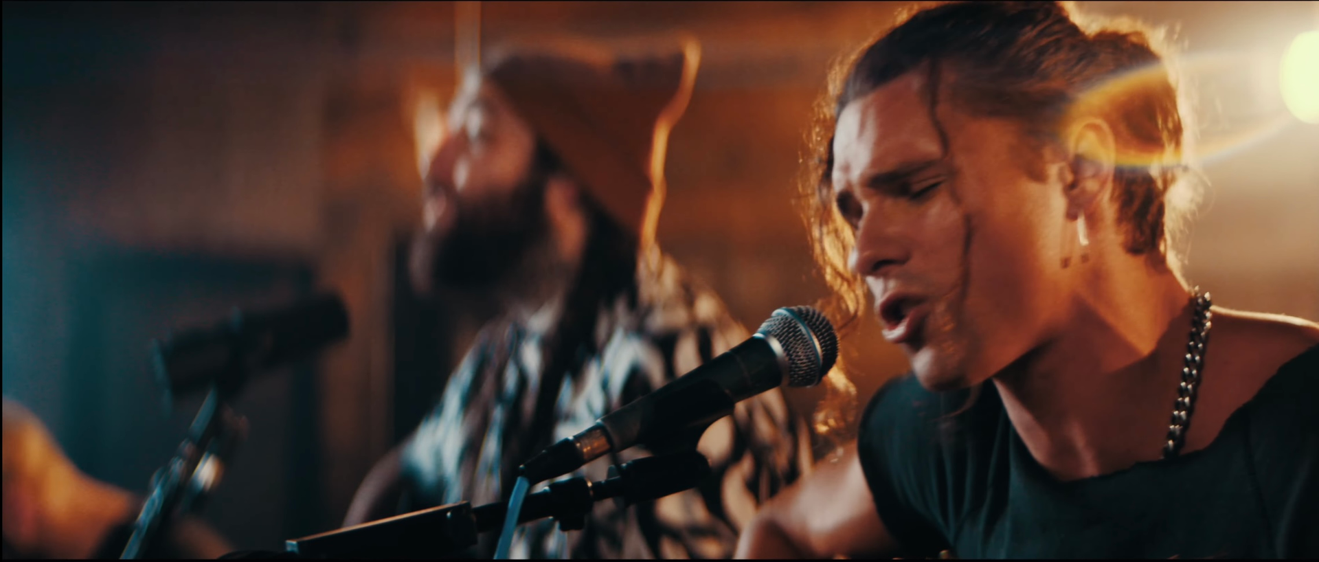 A man is singing into a microphone while another man plays a guitar.