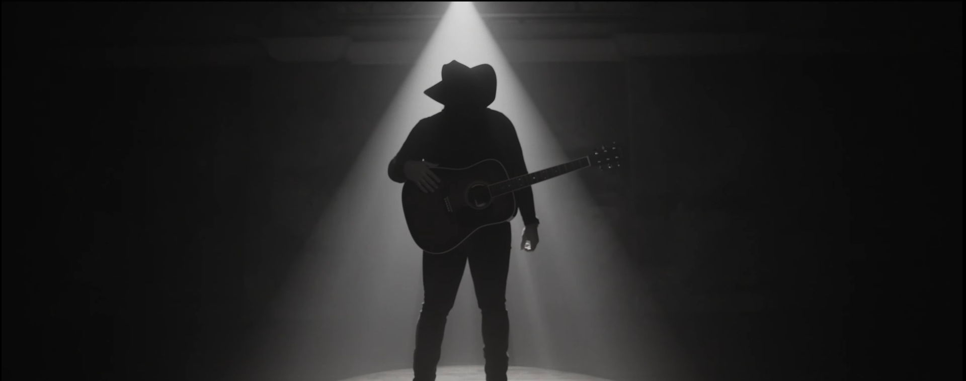 A silhouette of a person playing a guitar in a dark room.