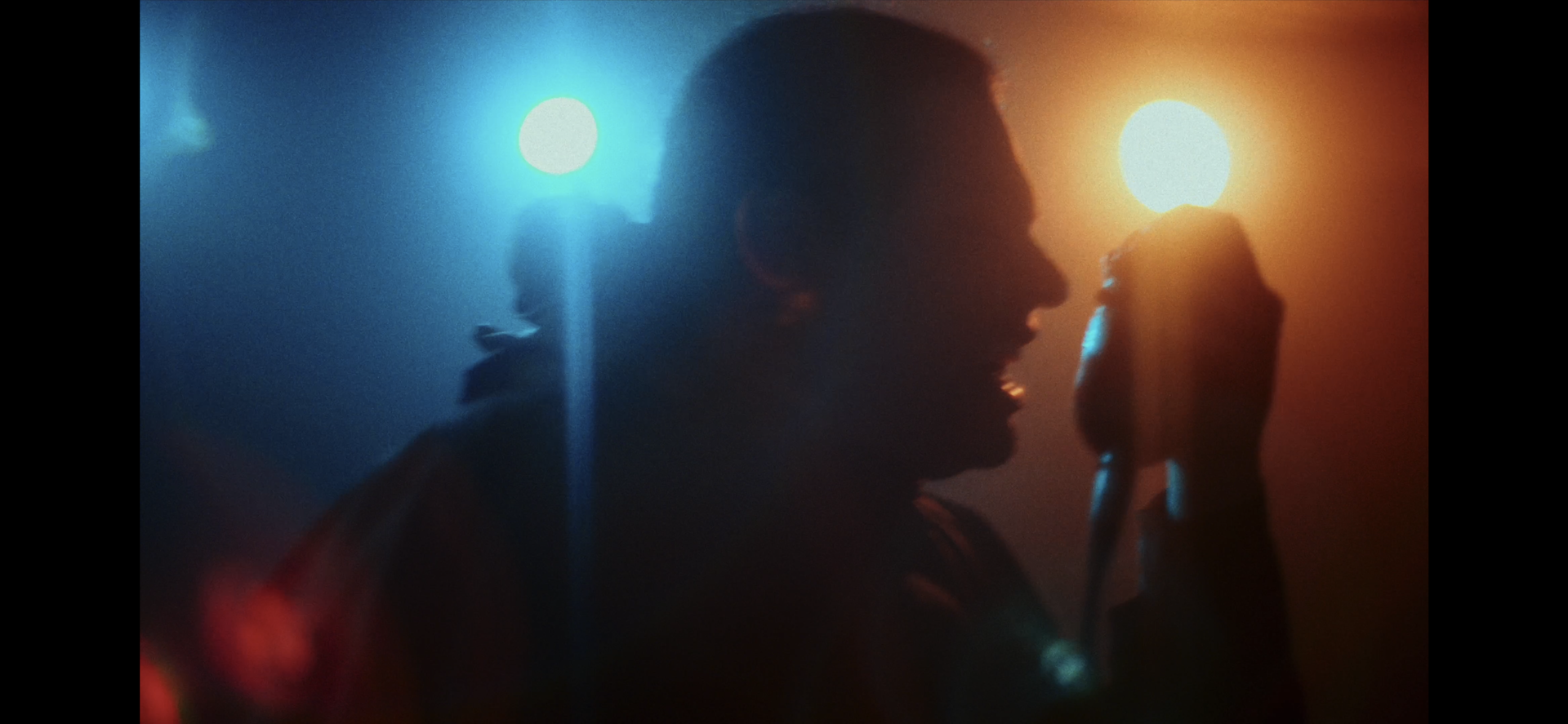 A man is singing into a microphone in a dark room.