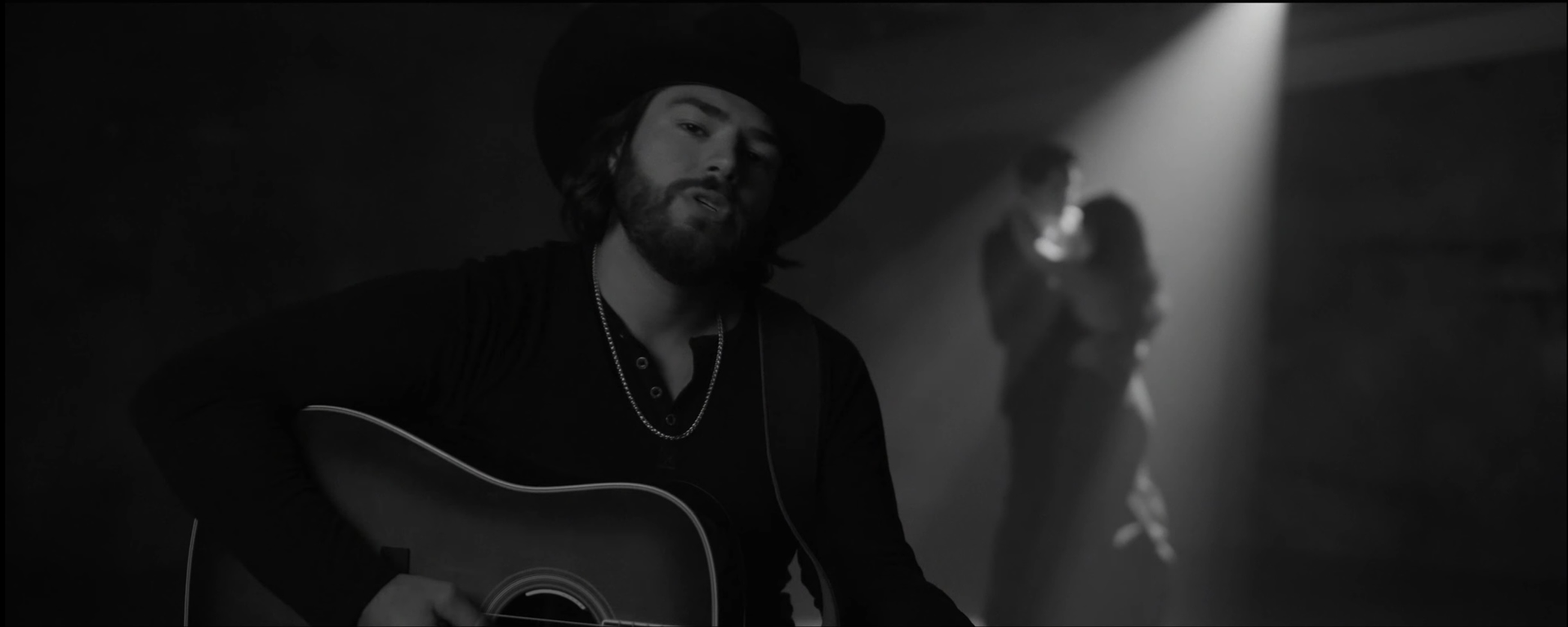 A man in a cowboy hat is playing a guitar in a dark room.