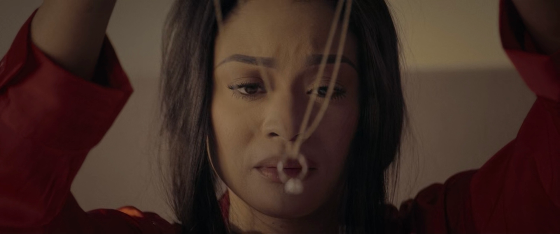 A woman in a red shirt is holding a string with a ring on it. From Dark Deceptions