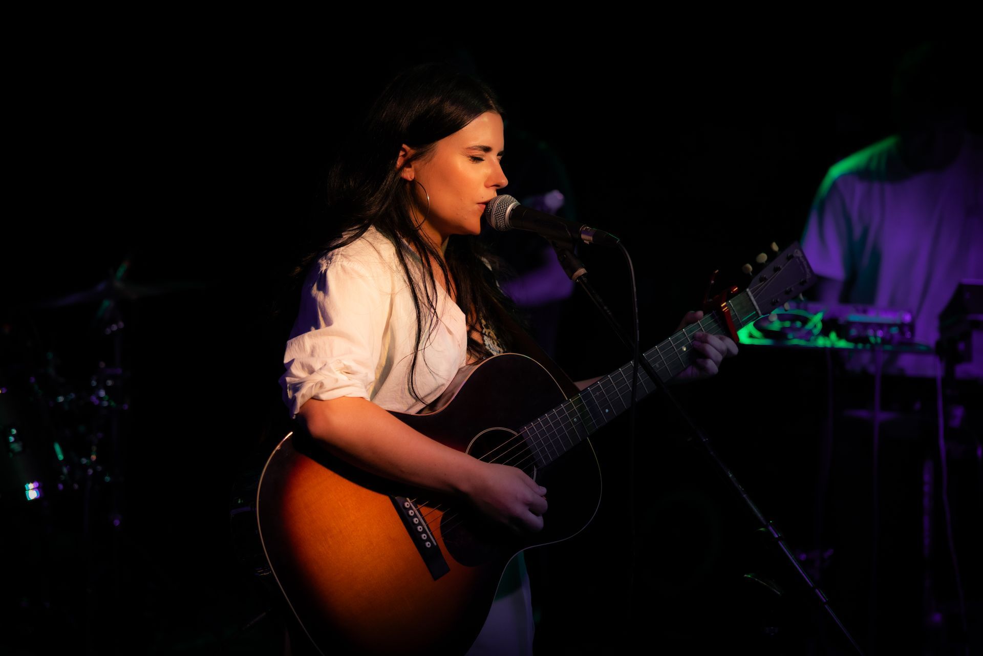 A woman is playing a guitar and singing into a microphone on a stage.