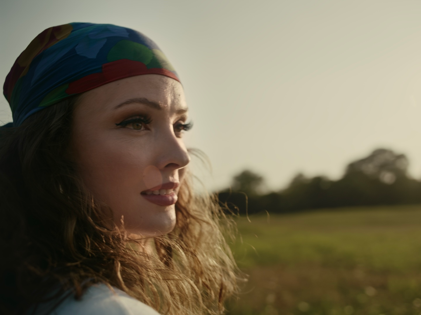 A woman wearing a colorful head scarf is standing in a field.