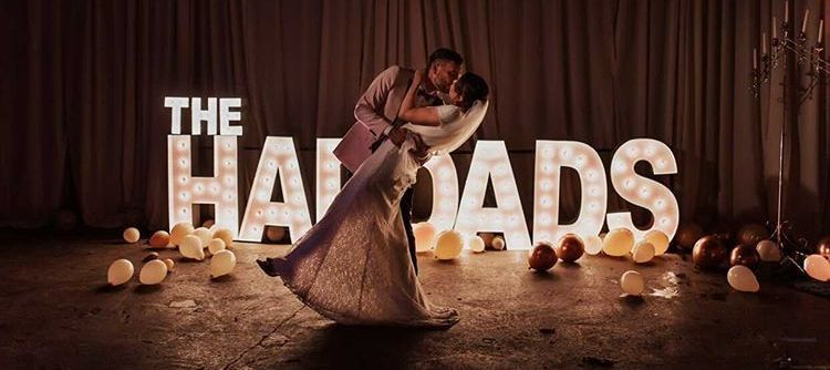 A bride and groom are dancing in front of a sign that says `` the haydads ''.