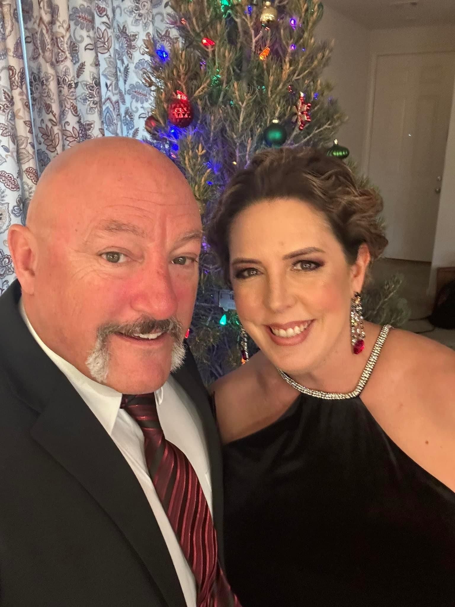 A man and a woman are posing for a picture in front of a christmas tree.