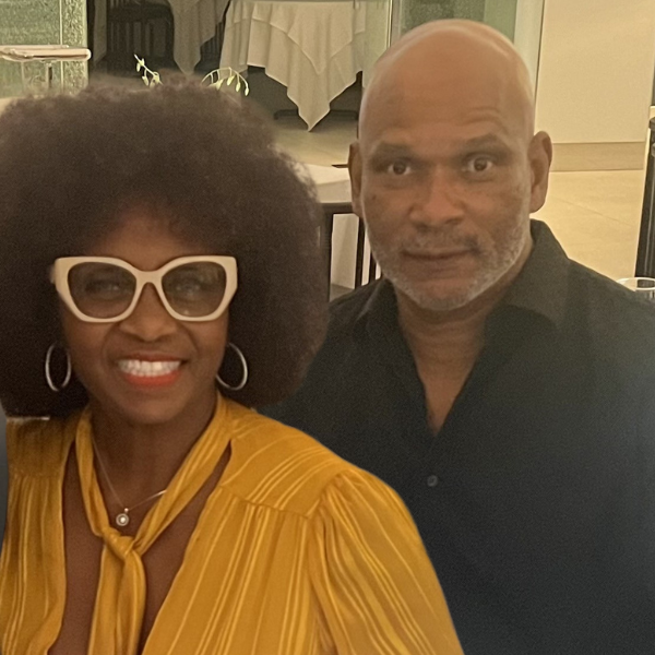 Woman with glasses and afro, next to a man with a shaved head, both smiling.
