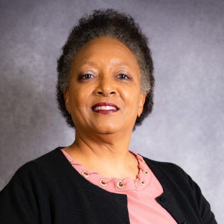 A woman in a pink dress is standing in front of a wall of flowers.