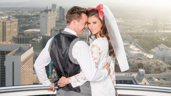 A bride and groom are posing for a picture on a balcony overlooking a city.