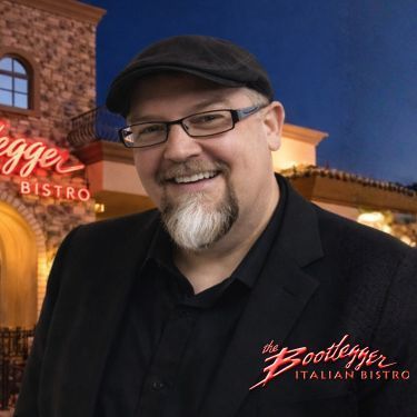 A woman wearing glasses and a black jacket is smiling