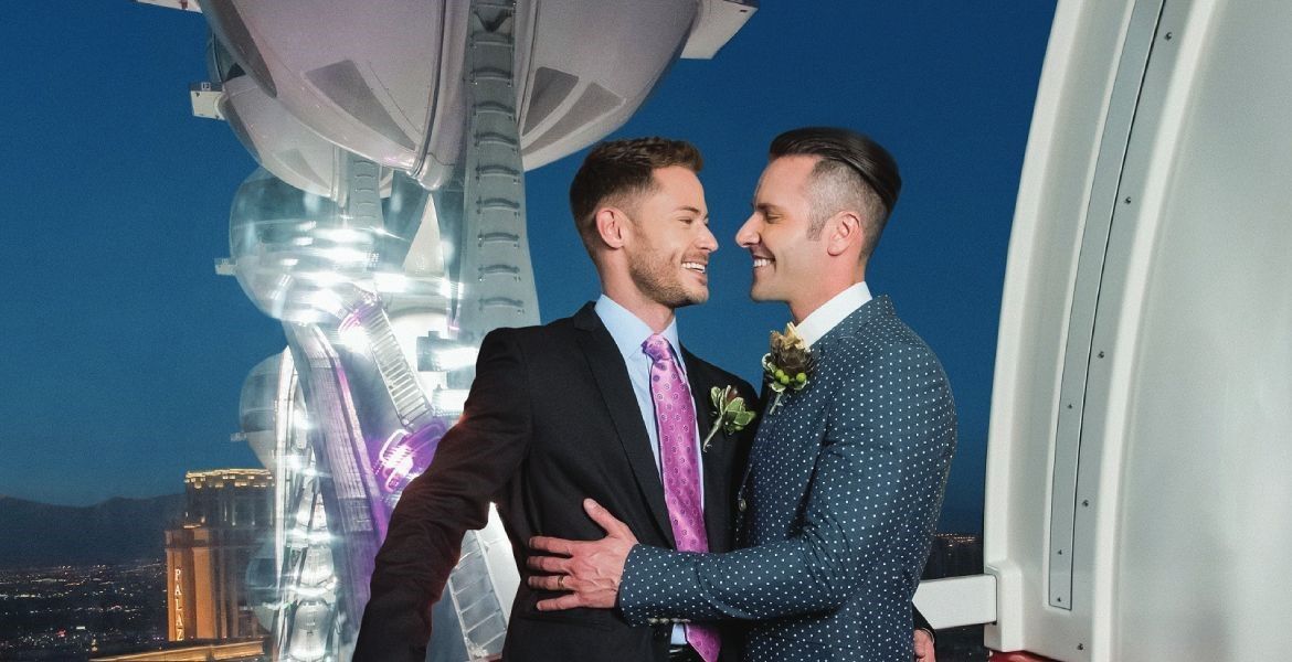 Two men in suits and ties are hugging each other in front of a ferris wheel.